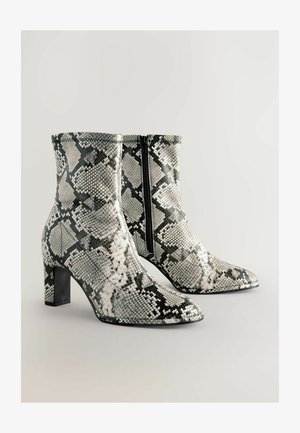 Čizme do gležnja s oštrim nožnim prstom u crno-bijelom uzorku zmijske kože, s bočnim zatvaračem i debelim potplatom za dodatnu stabilnost.
