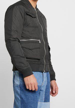 Chaqueta bomber de tejido gris oscuro, con bolsillos con cremallera, puños acanalados y un diseño ajustado. Presenta detalles de costura notables.