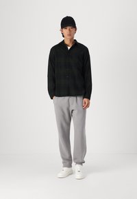 Black and green plaid button-up shirt, gray sweatpants, and white sneakers. The shirt has a collar and long sleeves; the pants are tapered.