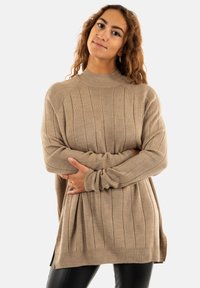 Pull en beige côtelé avec un col montant, des manches longues et des fentes sur les côtés. Texture lisse et coupe décontractée, idéale pour le superposition sur d'autres vêtements.