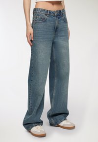 Jeans a gamba larga blu chiaro in tessuto denim con finitura sbiadita, caratterizzati da cinque tasche, chiusura con bottone e vestibilità rilassata.