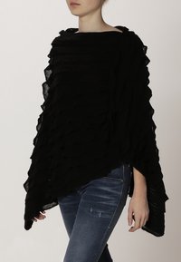 Svart poncho med en texturerad, lager-på-lager design. Mjukt material faller över axlarna, med en vid halsringning och ojämn fåll.