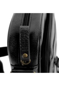 Bolso de piel negra con una superficie texturizada, que cuenta con un cierre de cremallera y un asa con marca que tiene un detalle de broche de metal dorado.