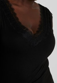 Top nero con scollatura a V, caratterizzato da un bordo in pizzo testurizzato. Realizzato in un tessuto morbido ed elasticizzato, ha una vestibilità aderente che enfatizza la silhouette.