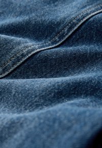 Close-up van blauw denimstof met zichtbare diagonale stiksels en textuurvol weefpatroon.
