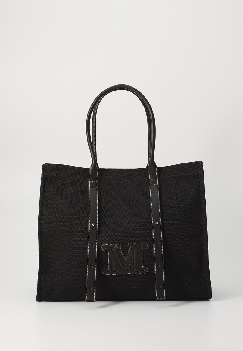 Black canvas tote bag with contrasting black leather handles, embossed "M" logo, and decorative stitching. Spacious and structured design.