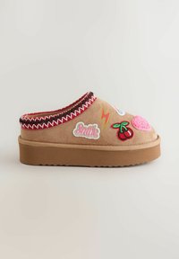 Tan suede slip-on shoes with a red-accented collar. Features colorful embroidered patches: cherries, hearts, and "Smile" text. Thick, textured sole.