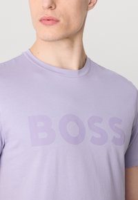 T-shirt lavande à manches courtes en coton doux, arborant un grand logo "BOSS" mat au centre de la même couleur.