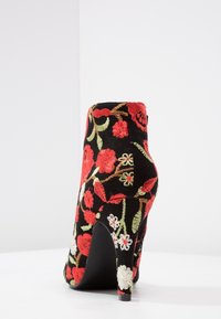 Schwarze High-Heel-Stiefelette mit buntem Blumenstickerei in Rot, Weiß und Grün, mit einer eleganten Silhouette und strukturiertem Stoff.