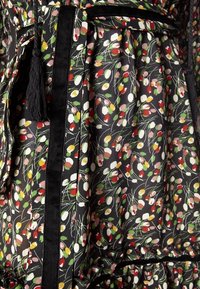 Blommönstrad tyg i svart med färgglada blommor. Inkluderar ett svart bälte och detaljer med tofsar. Har en samlad design med volangkanter.