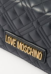 Kviltna črna usnjena torba s pozlačenim priznanjem "LOVE MOSCHINO". Zasnova z teksturiranim zaključkom in geometrijskim vzorcem.