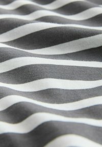 Detailní záběr měkké látky s vodorovnými černobílými pruhy vytvářejícími jemné, nestejné vlny po celé ploše.