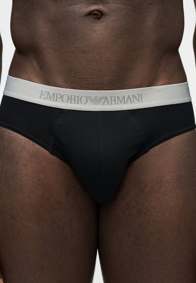 Αντρικός κορμός που φοράει μαύρα εσώρουχα με γκρι ζώνη μέσης που φέρει το λογότυπο Emporio Armani, σε απλό λευκό φόντο.