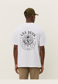 Witte katoenen t-shirt met een ronde zwarte grafische print op de achterkant met tekst en een geïllustreerd ontwerp. Casual fit met korte mouwen.