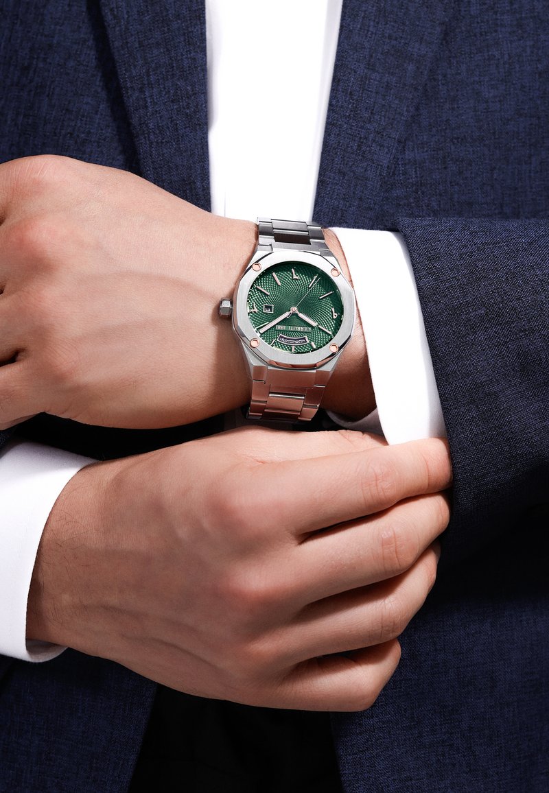 Reloj de acero inoxidable con una esfera texturizada verde, agujas plateadas y acentos en oro rosa, montado en una pulsera de metal plateado.