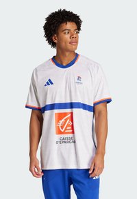 Hvid sportsjersey med blå accenter, der har en vandret blå stribe og et orange logo. Kortærmet med blå krave og branding.