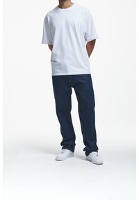 Camiseta de algodón blanca combinada con jeans de mezclilla azul oscuro. El conjunto incluye zapatillas blancas y presenta un diseño simple con un corte relajado.