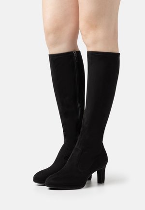 Bottes noires montantes en daim souple, avec un bout effilé et un talon carré. Détail de fermeture éclair sur le côté pour un enfilage facile. Texture lisse.