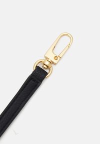 Černý kožený popruh s texturovaným povrchem, vybavený zlatou kovovou sponou a kroužkem, což umožňuje bezpečné připevnění.