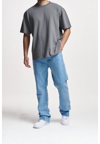 T-shirt in cotone grigio con vestibilità comoda, abbinato a jeans in denim blu chiaro con taglio loose. Sneakers bianche completano il look.