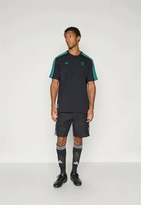 Melnas sporta apģērbs, kas sastāv no īsām piedurknēm kreklam ar tirkīza svītrām, atbilstošajiem šortiem un augstām zeķēm līdz ceļiem ar baltām svītrām.