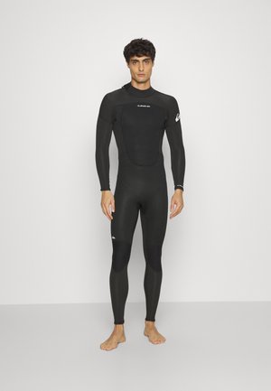 Survêtement noir avec des manches longues, un col montant et un tissu extensible. Comprend des panneaux renforcés aux genoux, des accents de logo sur les manches et la poitrine.