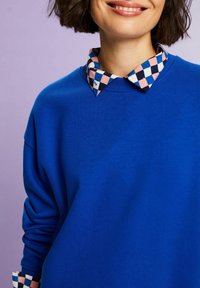 Sudadera azul de manga larga, con un cuello a cuadros en rosa, negro y blanco. Textura suave y un corte relajado.