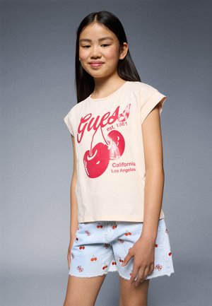 T-shirt rose clair avec graphique de cerises rouges et texte "Guess" ; accompagné de shorts bleu clair avec des motifs de cerises brodés.
