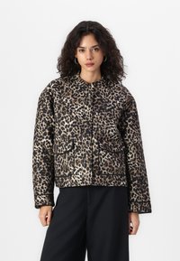 Veste à imprimé léopard avec un col rond, des poches avant et une texture matelassée. La palette de couleurs comprend des nuances de beige, noir et des accents de crème.
