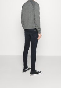 Sudadera gris texturizada de manga larga, combinada con jeans azul oscuro y zapatillas negras, vista desde la parte posterior.