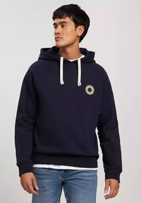 Granatowy polar z kapturem na sznurki, z okrągłym emblematem na klatce piersiowej. Wykonany z miękkiego materiału, o regularnym kroju i ściągaczach przy mankietach.