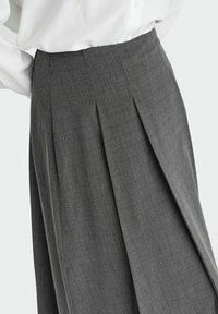 Falda plisada gris hecha de tejido texturizado con un sutil patrón de cuadros. Presenta una cintura alta y un diseño estructurado.