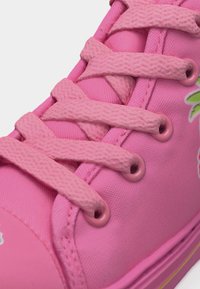 Κοντινό πλάνο ενός ροζ αθλητικού παπουτσιού με υφασμάτινο επάνω μέρος, ροζ υφασμάτινα κορδόνια με υφή περασμένα μέσα από ροζ μεταλλικά παρδαλάκια.