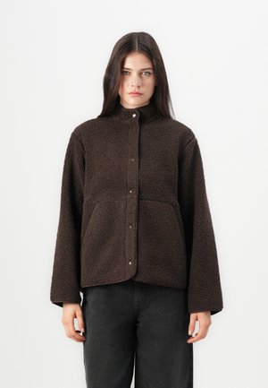 Brown fleece jacket with a high collar, front snap buttons, and two side pockets. Features a textured, plush surface and relaxed fit.
