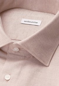 Camicia collared rosa chiaro con tessuto testurizzato, dotata di un bottone bianco e di un'etichetta con la scritta "seidensticker" in un font pulito.
