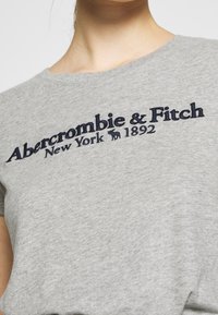 Grå bomulds t-shirt med marineblå broderet tekst: "Abercrombie & Fitch New York 1892." Rund hals og blød tekstur.