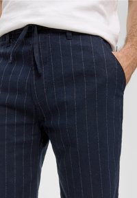 Marine gestreepte broek met lichtgrijze streepjes, gemaakt van een zachte stof; voorzien van een elastische tailleband en zijzakken.