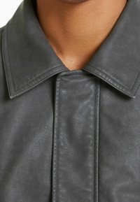 Szara skórzana kurtka z szerokim kołnierzem, gładką teksturą i szczegółowym przeszyciem wzdłuż przodu i brzegów kołnierza.