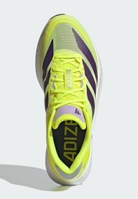 Scarpa sportiva gialla brillante con accenti viola, caratterizzata da una tomaia in mesh traspirante, punta arrotondata e suola imbottita. "ADIZERO" in evidenza.