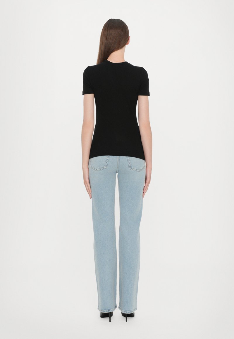 T-shirt nero a maniche corte abbinato a jeans dritti azzurri con vita alta e sottili tasche posteriori. Tacchi neri completano il look.
