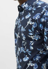 Camicia blu marina con bottoni e motivo floreale in diverse tonalità di blu. Presenta un colletto strutturato e una texture liscia in cotone.