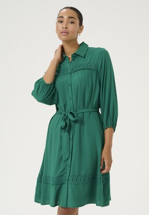 Abito verde a camicia con vestibilità rilassata, maniche 3/4, cintura in vita e dettagli in pizzo lungo il corpetto e l'orlo. Tessuto morbido.