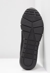 Semelle de chaussure en caoutchouc noir avec des motifs de bande de roulement et des zones de grip texturées sur un fond blanc.