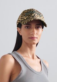 Leopard print baseball cap with green embroidered "AMOUR," featuring a curved visor and textured fabric. Worn by a model with straight hair.