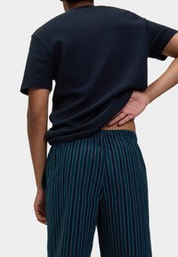 Marineblauwe textuur korte mouwen t-shirt gecombineerd met donkergroene gestreepte broek. De broek heeft een relaxte pasvorm en een elastische tailleband.