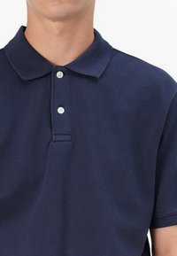 Mørkeblå polotrøye laget av teksturert stoff, med klassisk krage, to knapper og en avslappet passform.