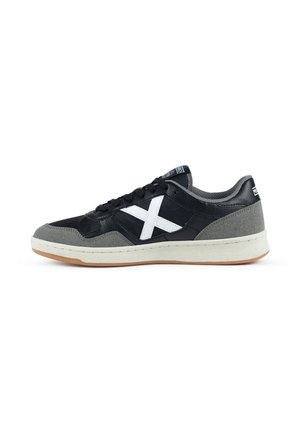 Zapatilla deportiva baja con parte superior negra y gris, logo X blanco en el lateral, entresuela blanca, suela de goma color marrón y cordones negros.