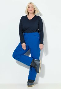 Modré venkovní kalhoty s rovným střihem, elastickým pasem a bočními kapsami, doplněné černým tričkem s dlouhým rukávem a černými botami.