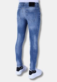 Vervaagde blauwe skinny jeans hebben twee achterzakken en een zwart merkje op de tailleband, gecombineerd met witte sneakers met zwarte accenten.