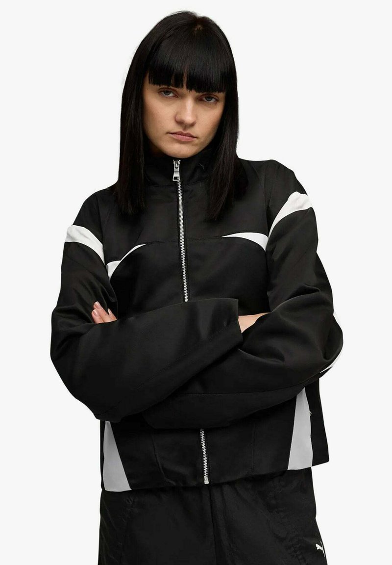 Giacca nera con zip, dettagli bianchi, collo alto e maniche larghe. Tessuto liscio, design corto, con pannelli laterali a contrasto.